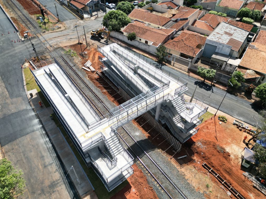 Vista aérea de uma passarela pedonal sobre linhas férreas em área residencial.