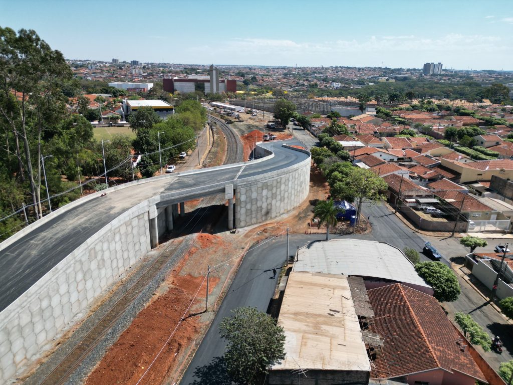Viaduto curvo elevado passando sobre trilhos em bairro urbano.