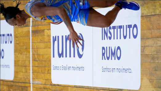 Atleta correndo em quadra, com placas do Instituto Rumo ao fundo.