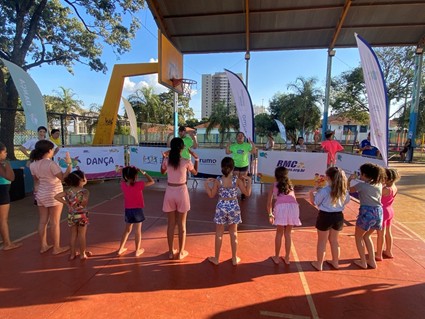 Crianças participam de atividade esportiva em uma quadra coberta, acompanhadas por monitores.